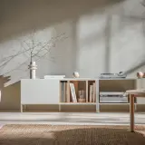 Miękkie światło pada na ściany w kolorze kaszmirowym, oświetlając salon z minimalistyczną komodą i wygodną sofą.