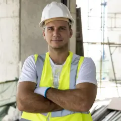 Kierownik budowy w kamizelce odblaskowej i kasku, z rękami skrzyżowanymi na piersi. Zastanawiasz się, ile kosztuje kierownik budowy?