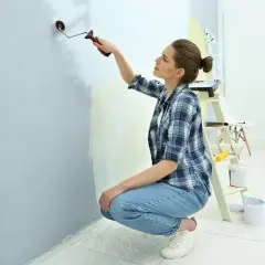 Kobieta w kratę i jeansach wykonuje malowanie ściany na jasny kolor.