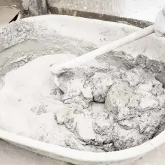 Mieszanie zaprawy z wapna palonego w dużej misie. Ręka w rękawicy miesza gęstą, szarą masę.
