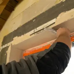 Budowlaniec wygładza tynk nad oknem, tworząc gładkie glify.