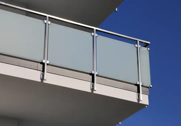 Nowoczesne mocowanie balustrady od czoła z matowego szkła i stali nierdzewnej, z widocznym niebieskim niebem w tle.