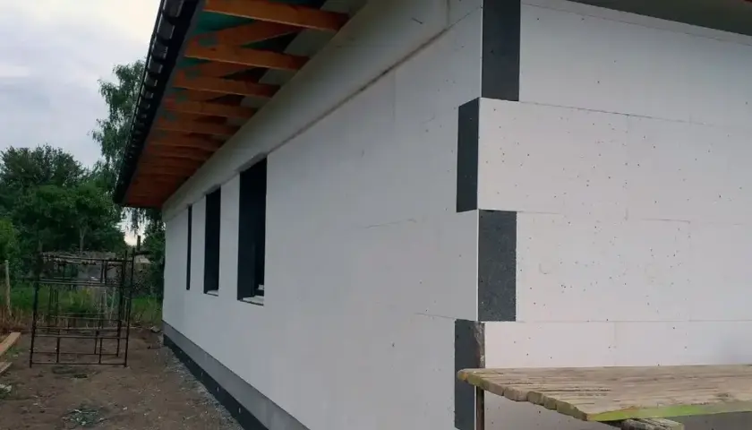 Budynek z białymi płytami termoizolacyjnymi, widoczne czarne elementy narożne i okna.