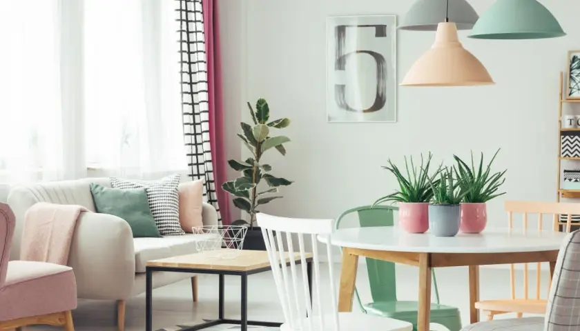 Przytulny salon z sofą i fotelem w **kolorach pastelowych**. W centralnym punkcie stoi okrągły stół z roślinami w doniczkach.