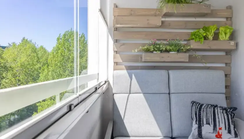 Przytulna loggia z szarą sofą, poduszką z liskiem i zielenią na drewnianej ściance.