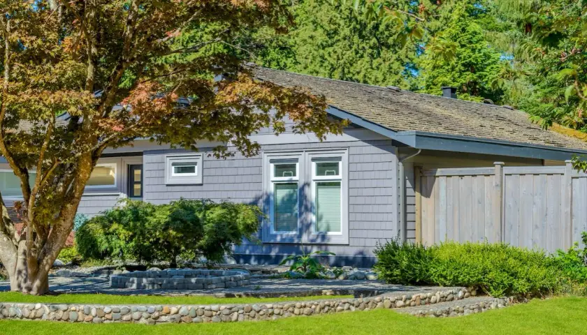Szary bungalow z dwoma oknami i drzewem klonu przed nim. To idealny przykład, bungalow co to za dom.