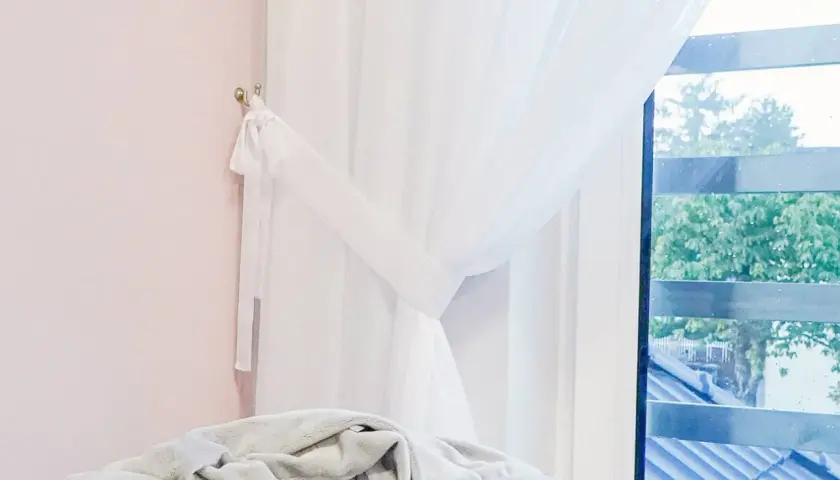 Białe firany upięte wstążką na jasnoróżowej ścianie, widok przez okno.