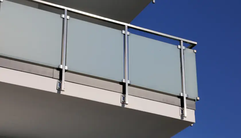 Nowoczesne mocowanie balustrady od czoła z matowego szkła i stali nierdzewnej, z widocznym niebieskim niebem w tle.