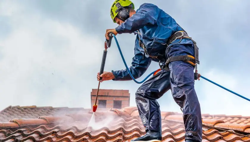 Pracownik w kasku myje dach myjką ciśnieniową. Sprawdź, jaka jest mycie dachu cena i odzyskaj blask swojej posesji.