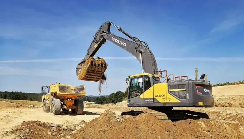 Koparka Volvo zasypuje wykop, przygotowując teren pod ułożenie rur. Cennik usług bez materiału.