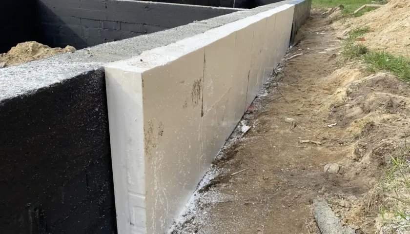 Izolacja fundamentów z białych płyt styropianowych przylega do czarnych bloczków betonowych fundamentowych.