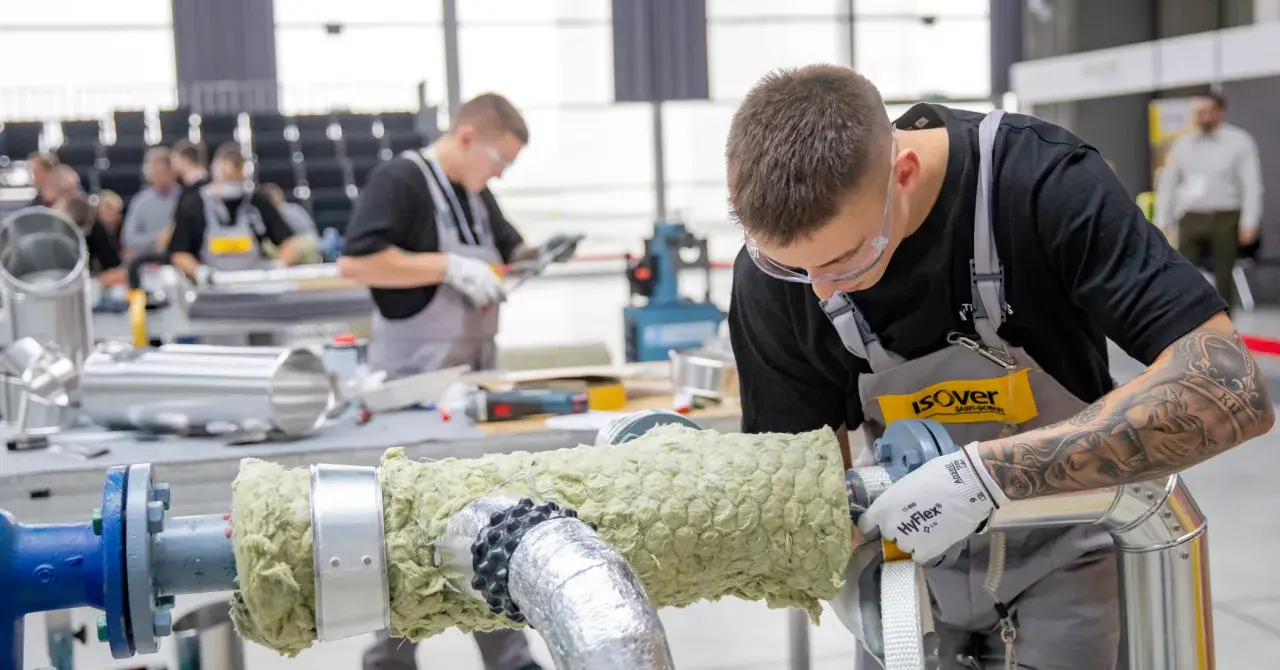 Młody mężczyzna w okularach ochronnych i fartuchu pracuje nad izolacją rury. Dbałość o detale i precyzja zapewniają dobrą adhezję materiału izolacyjnego.