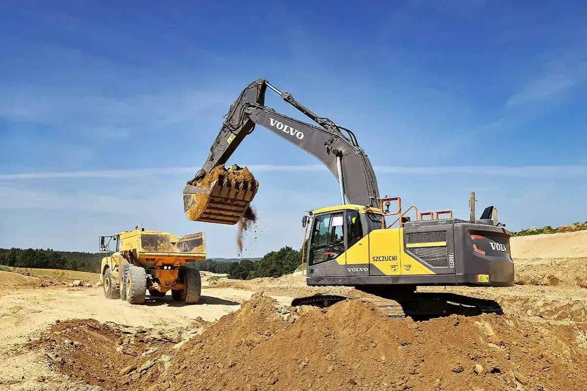 Koparka Volvo zasypuje wykop, przygotowując teren pod ułożenie rur. Cennik usług bez materiału.