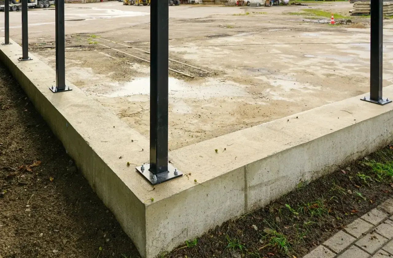 Fundament gotowy, szybki beton czeka na dalsze prace. Widać słupy konstrukcyjne i plac budowy w tle.
