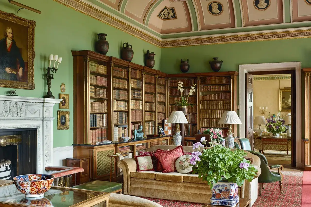 Elegancki salon w stylu angielskim z zielonymi ścianami, regałami pełnymi książek, kominkiem i wygodną kanapą.